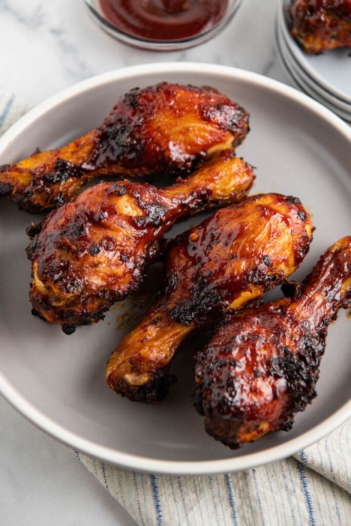 Four air fryer chicken legs with sauce sitting on a gray plate.