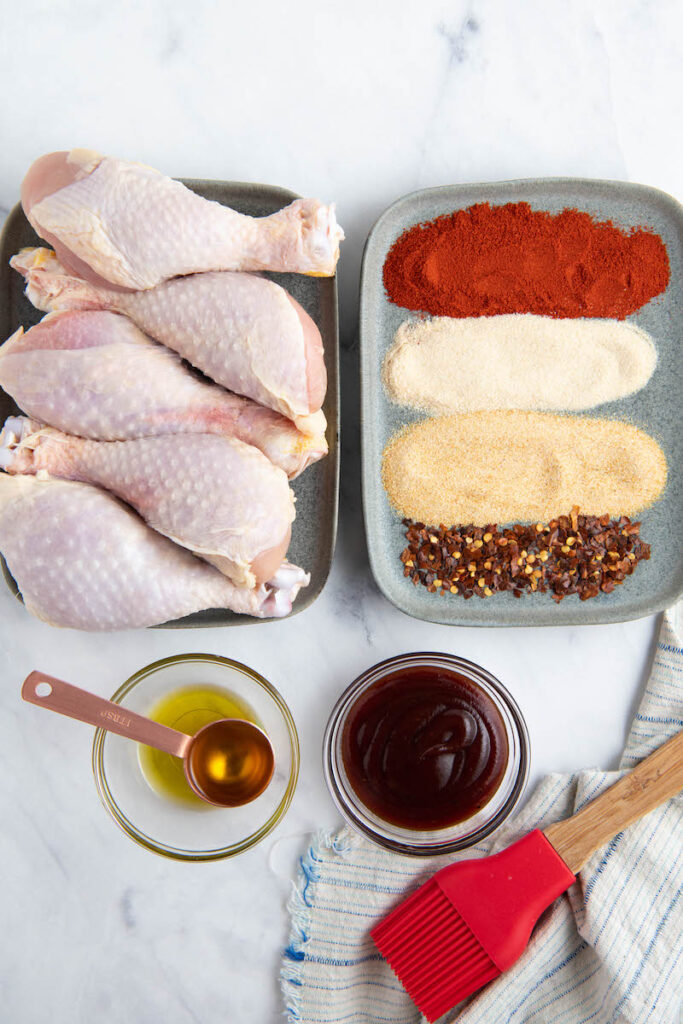 Ingredients in bowls with a plate of chicken drumsticks.