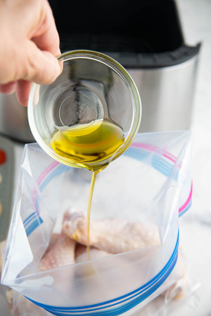 Olive oil poured over chicken drumsticks in a bag.