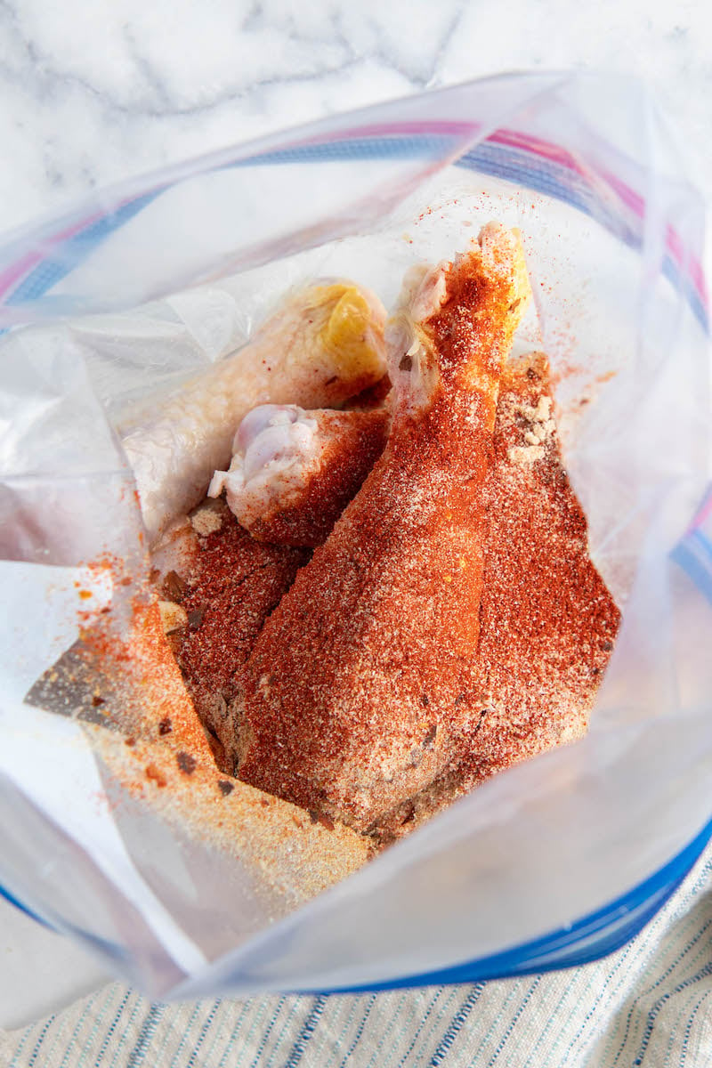 Chicken legs in a ziplock bag with seasonings all on top.
