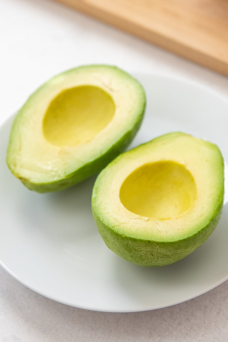 Two halves of an avocado without the pit on a white plate.