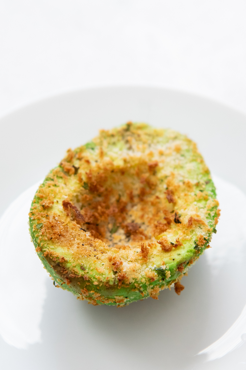 A half on an air fried avocado on a white plate.