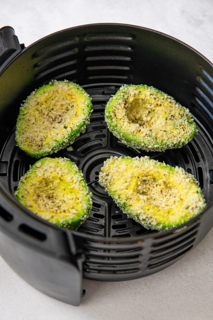 Breadcrumb coated avocado halves are in a black air fryer basket.