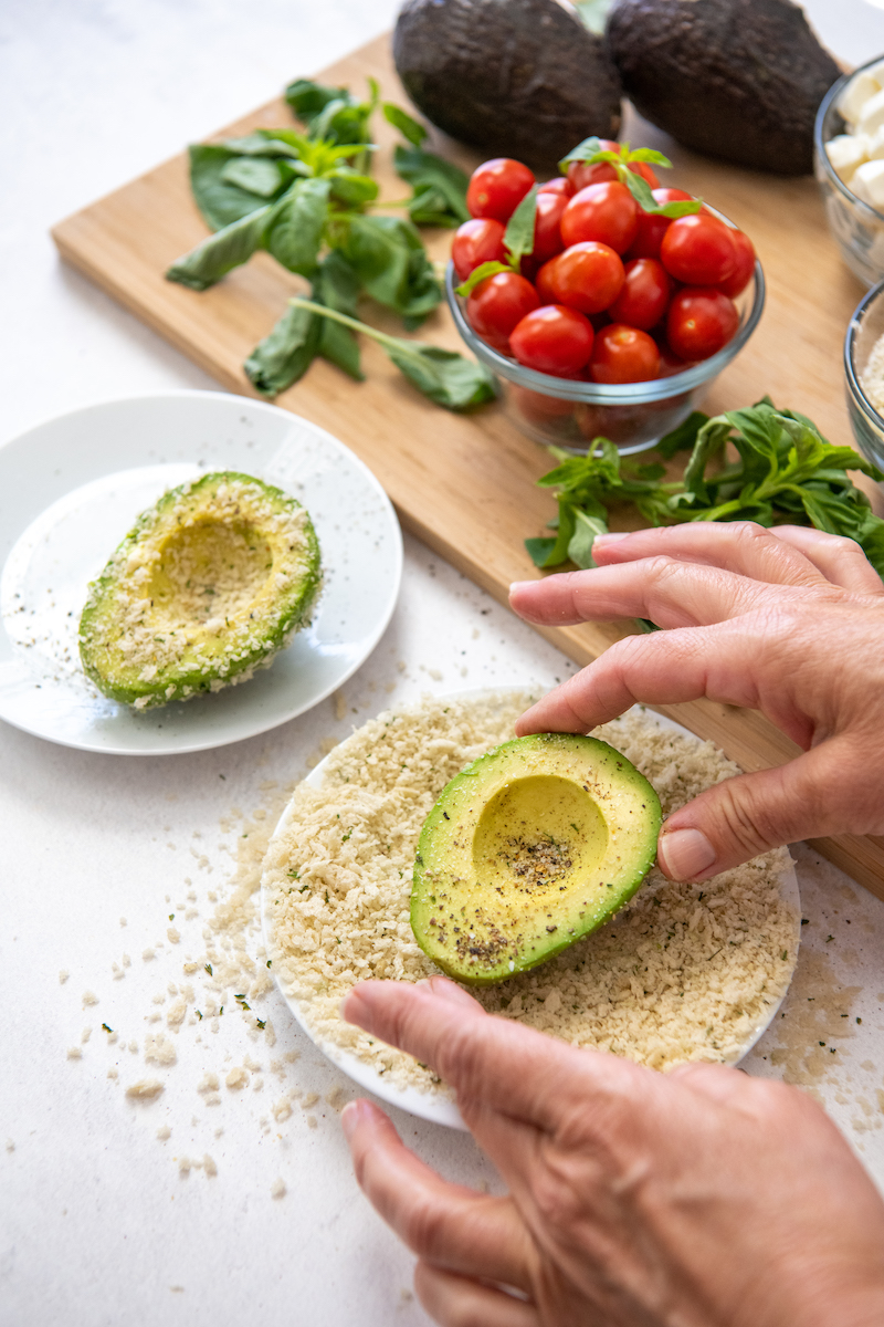 Avocado halves are rolled in breadcrumbs on a white plate.