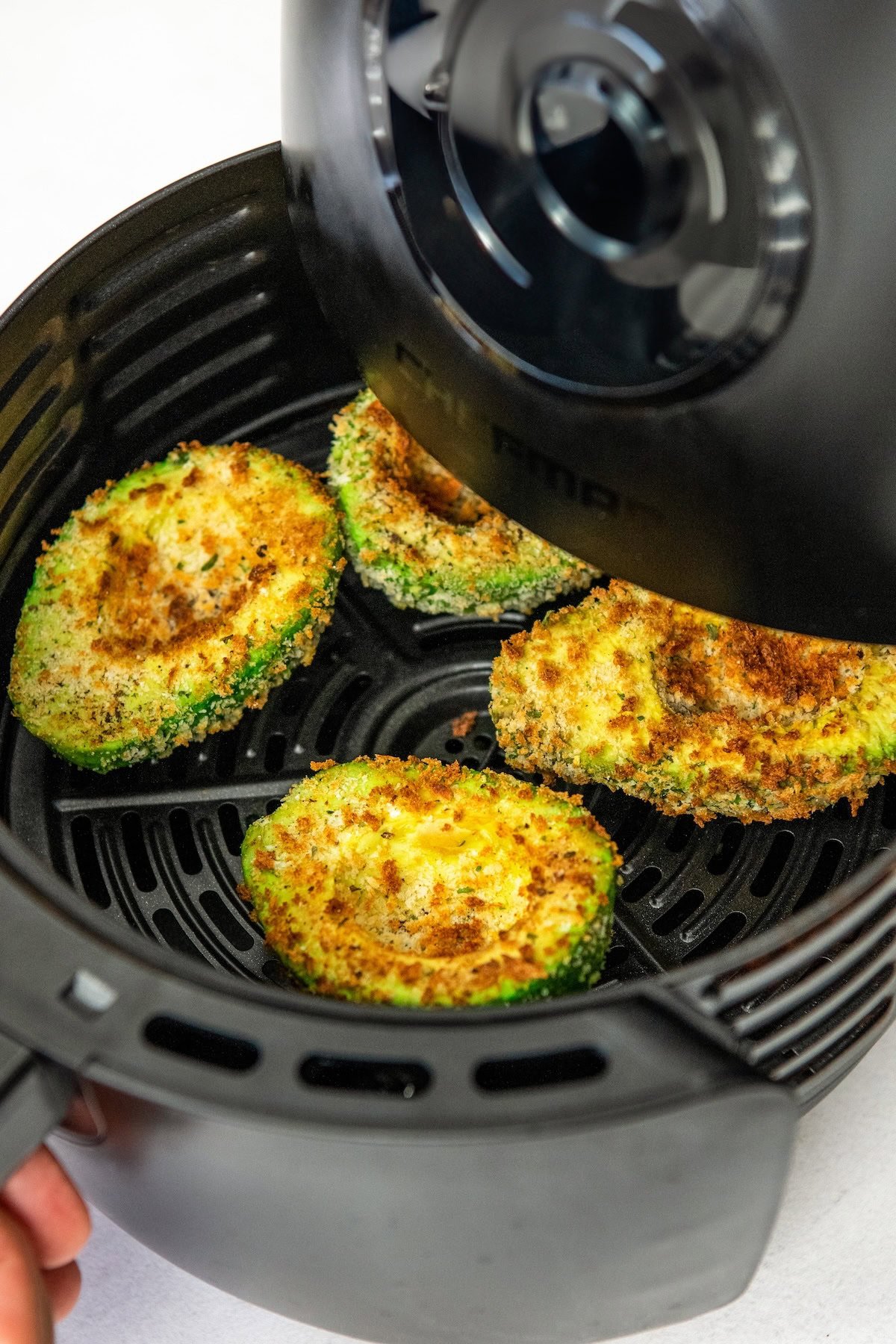 Crispy air fryer avocado halves in an air fryer basket.