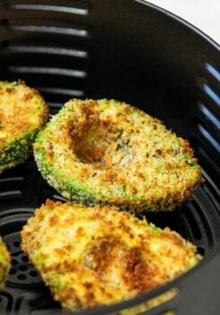 Crispy, golden brown air fried avocado halves in an air fryer basket.