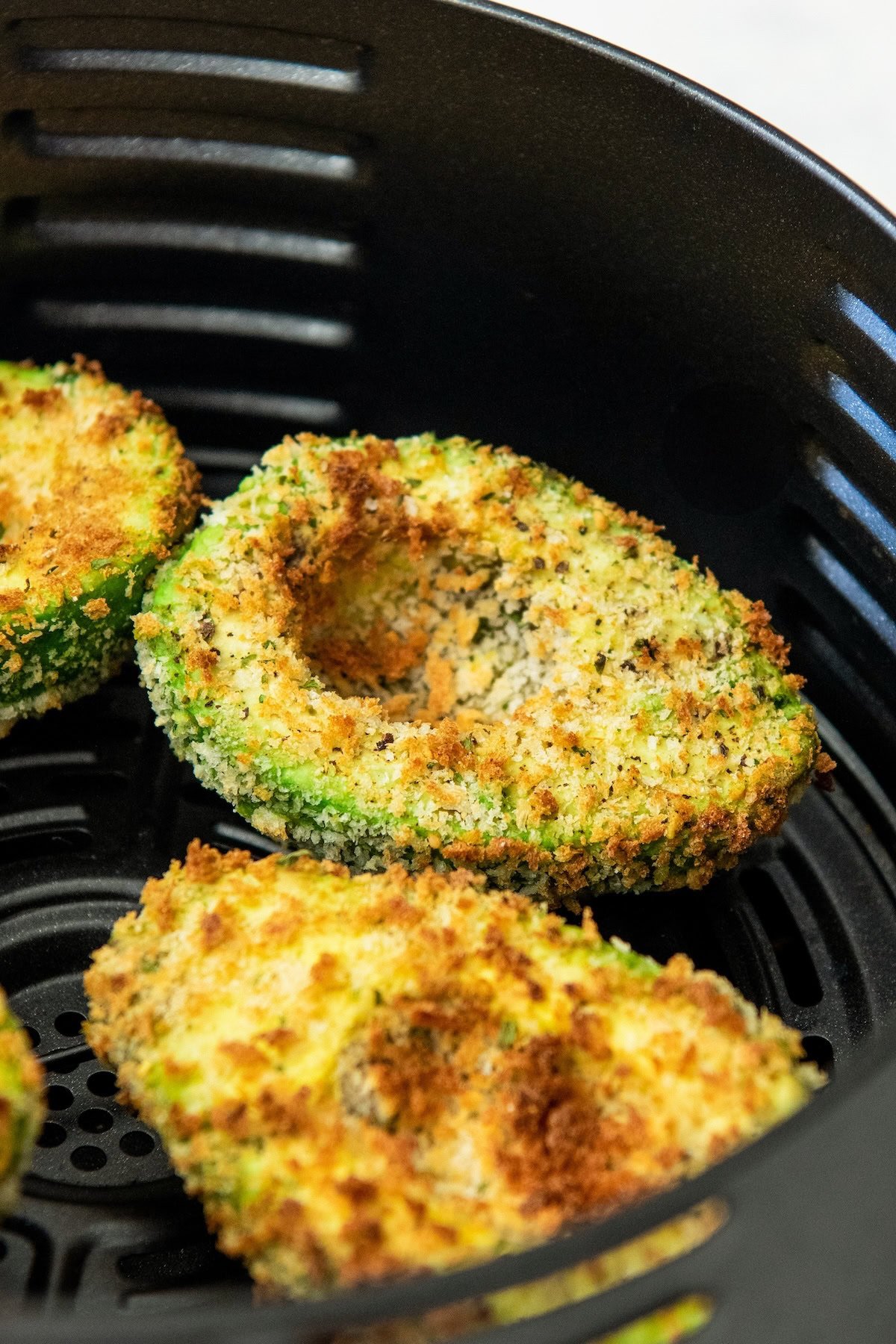 Crispy, golden brown air fried avocado halves in an air fryer basket.