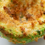 Up close image of A half on an air fried avocado on a white plate.