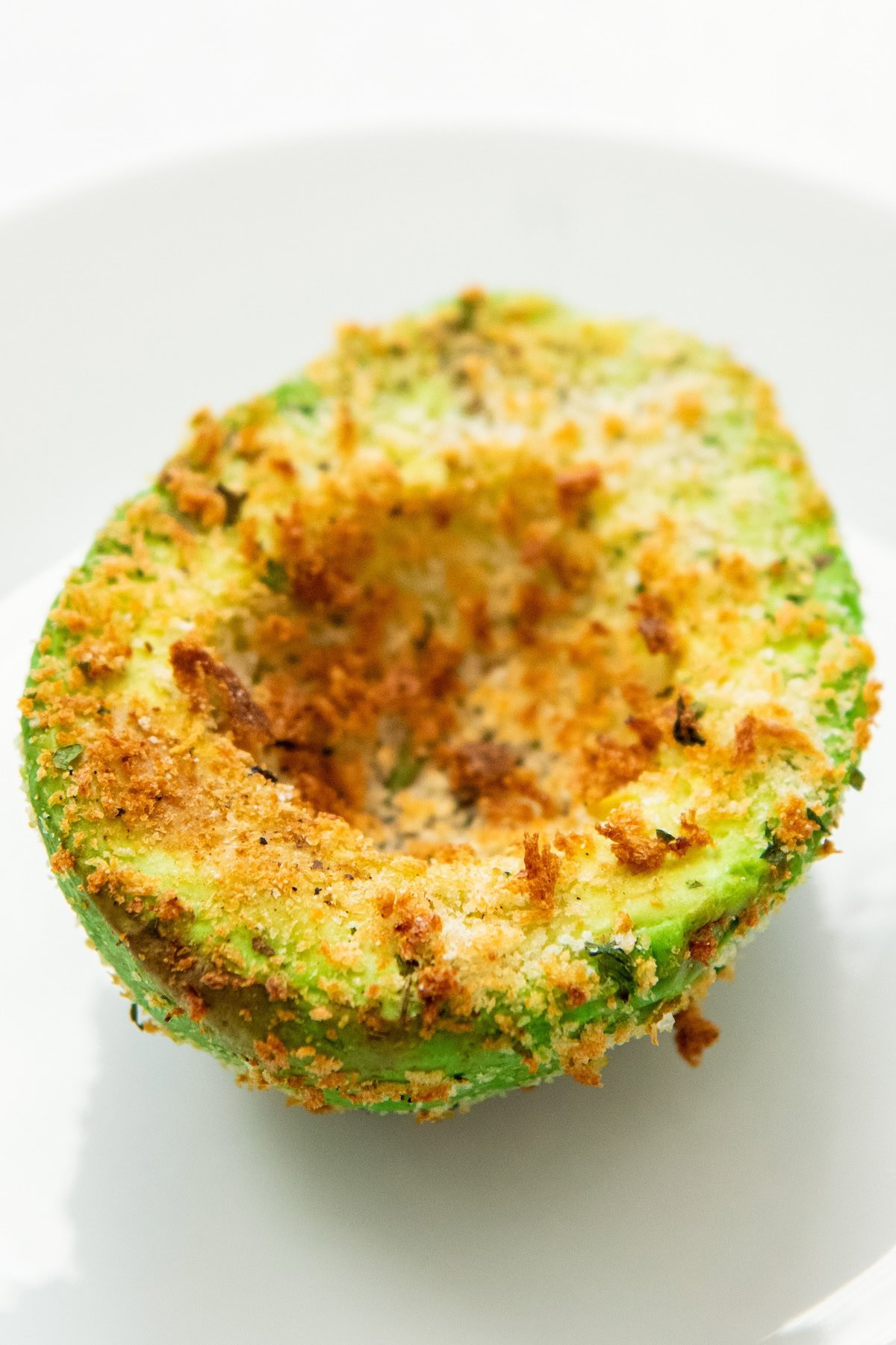 A crispy air fried avocado half is on a white plate.