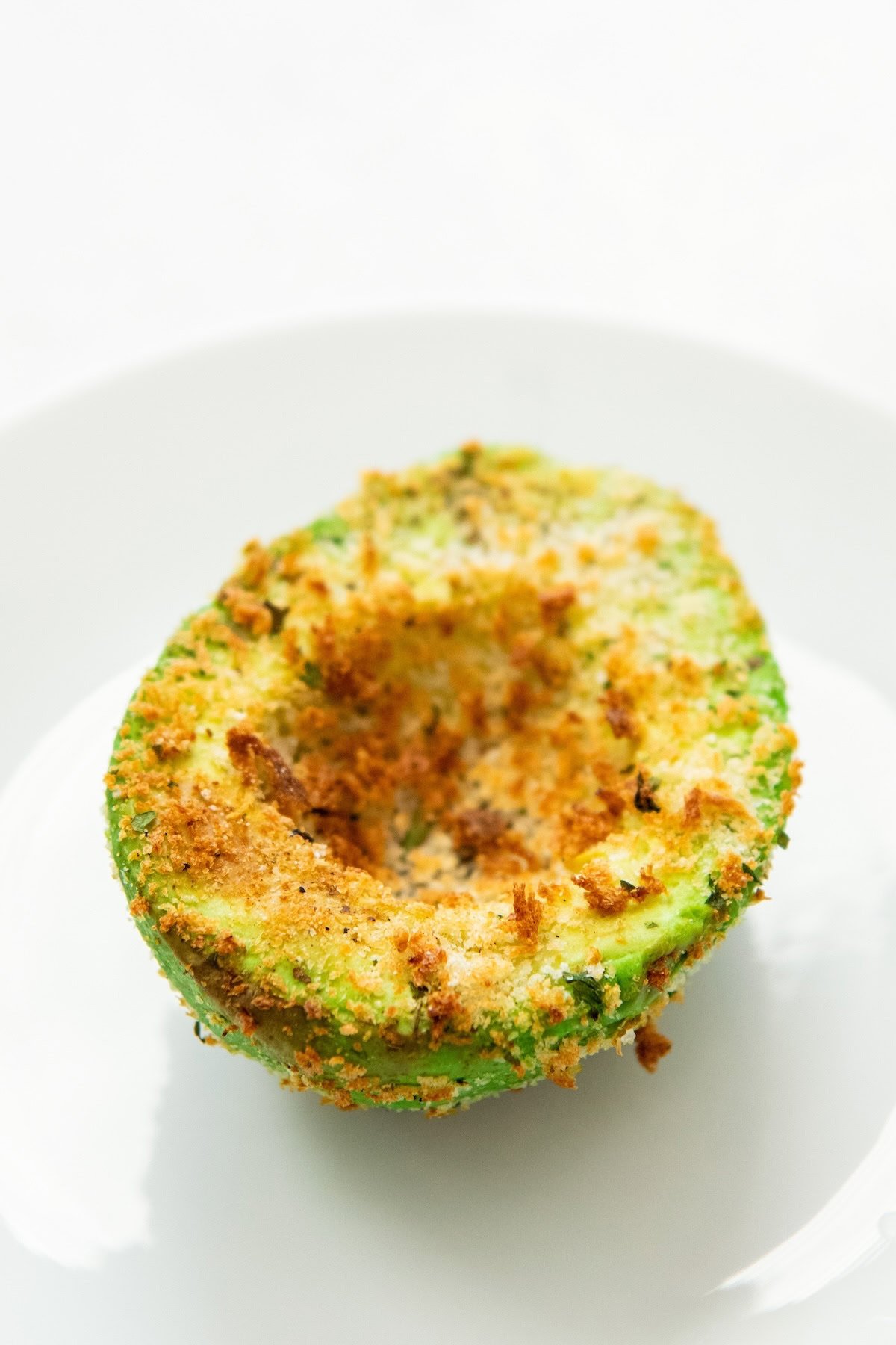 A vibrant green avocado half has been coated with seasoned breadcrumbs and air fried to golden crispy perfection.