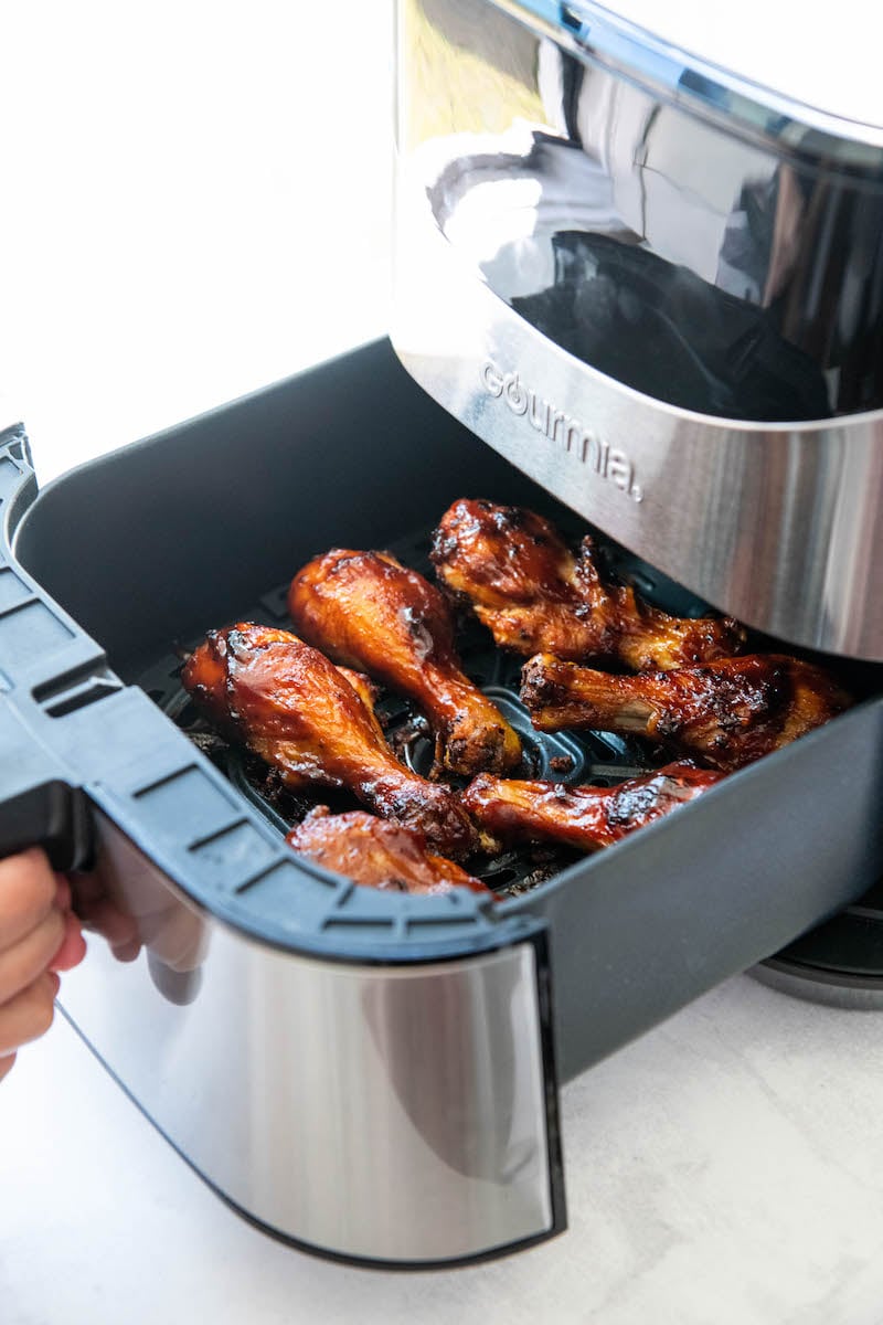 Chicken legs in an air fryer basket being pulled out of the air fryer.