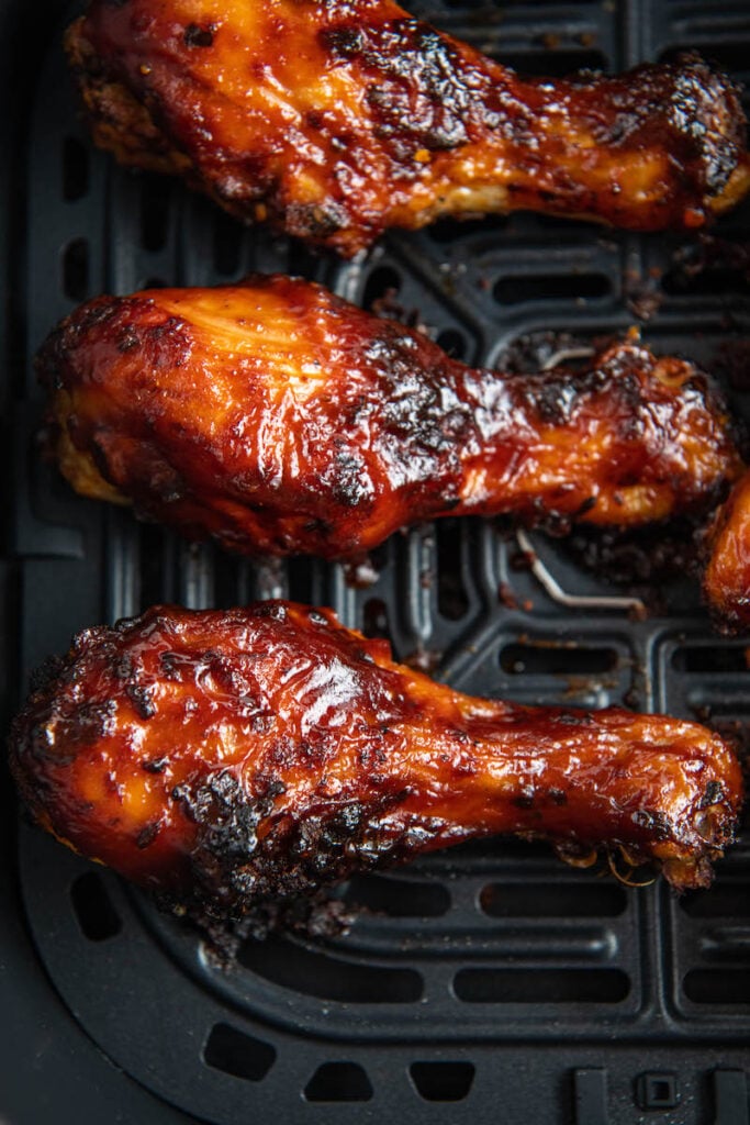 Up close image of three Air Fryer Chicken Drumsticks in a air fryer basket.