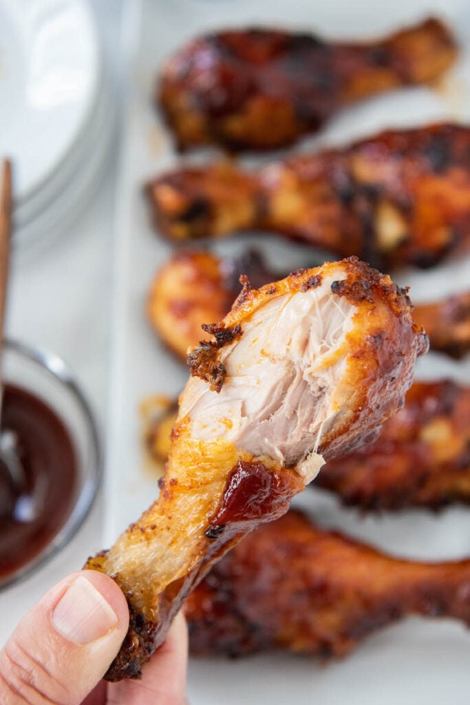 Chicken leg being held with a bite taken out of it.