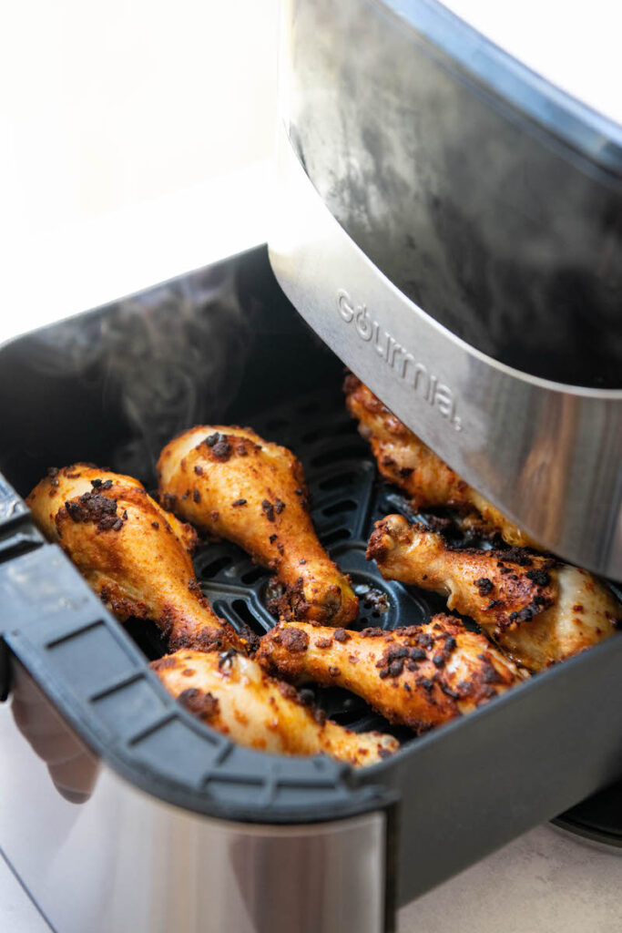 Air fryer chicken legs in a air fryer basket with steam coming off.