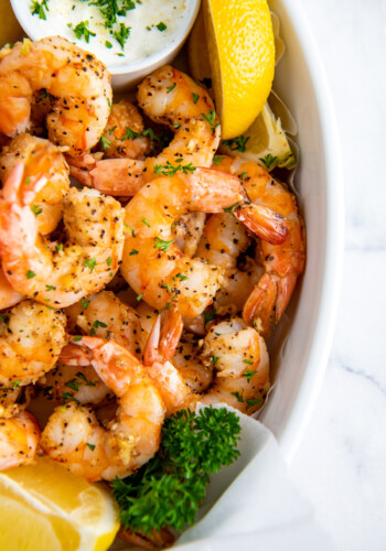 Air fried shrimp are placed in a white serving dish with a slice of lemon.