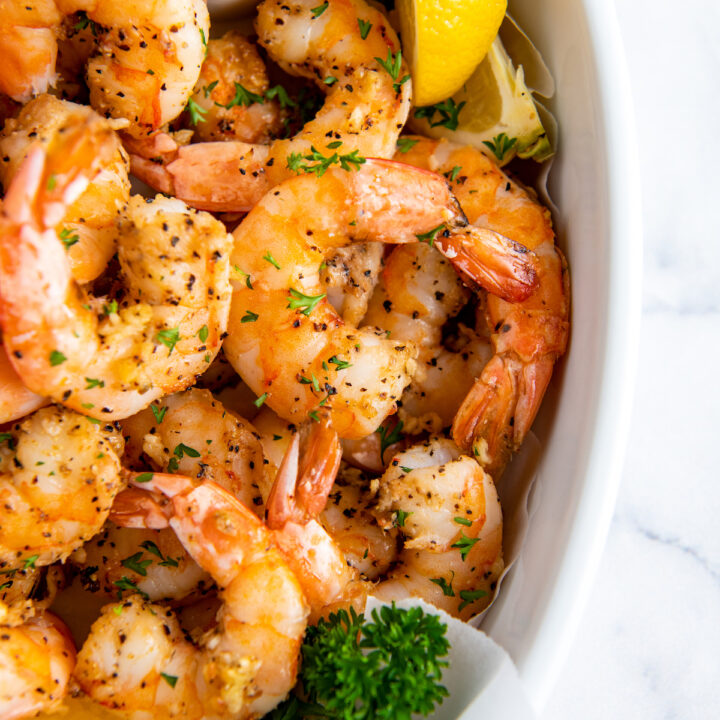 Air fried shrimp are placed in a white serving dish with a slice of lemon.