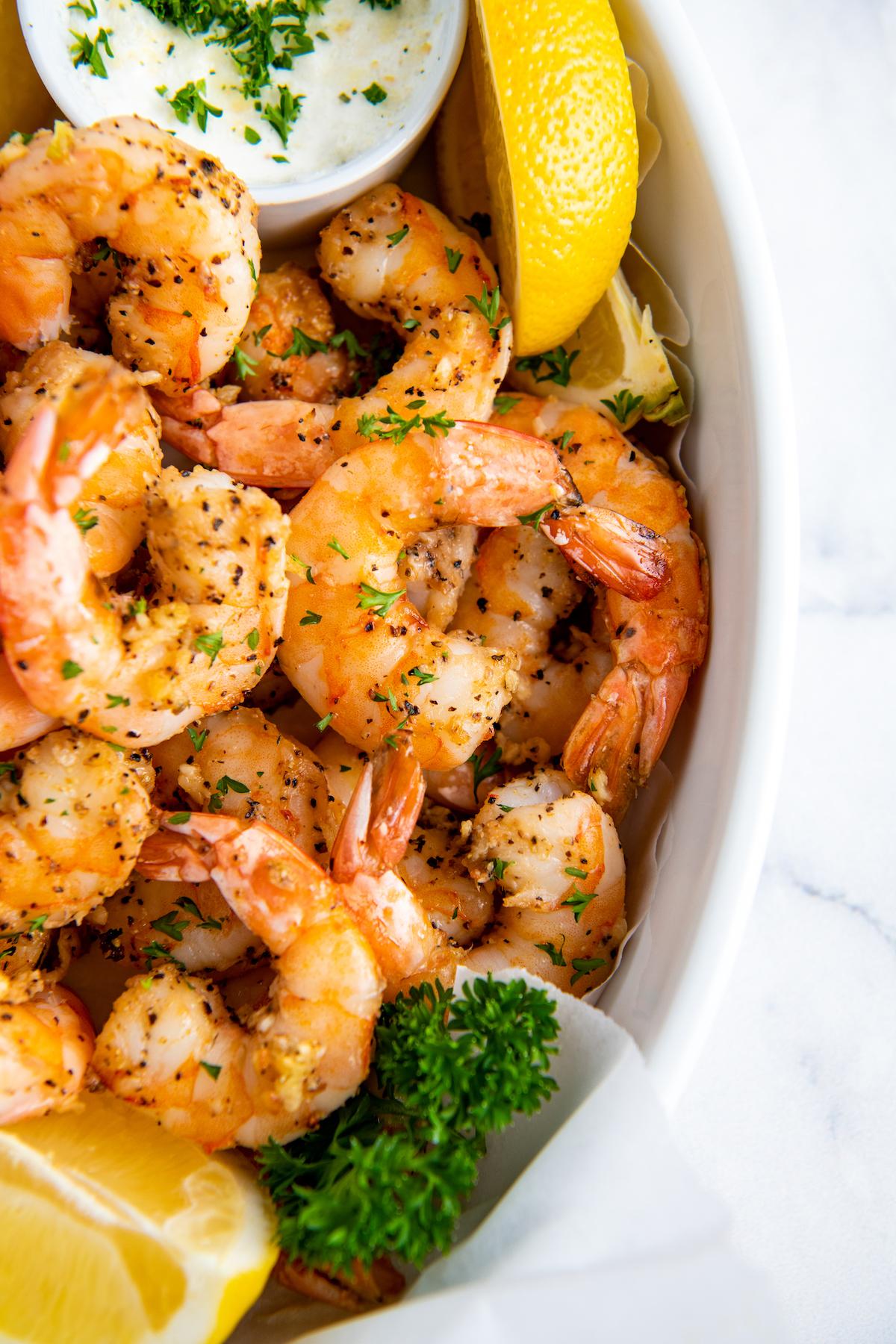 Air fried shrimp are placed in a white serving dish with a slice of lemon.