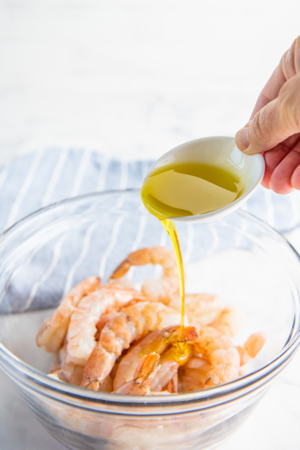 Olive oil is being drizzled onto uncooked shrimp.