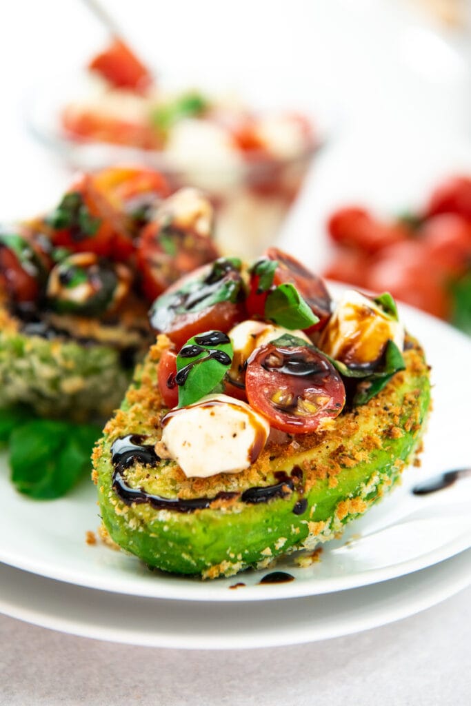 Two stuffed avocados are on a white plate, ready to be eaten.