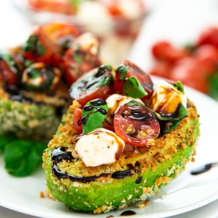 Two stuffed avocados are on a white plate, ready to be eaten.
