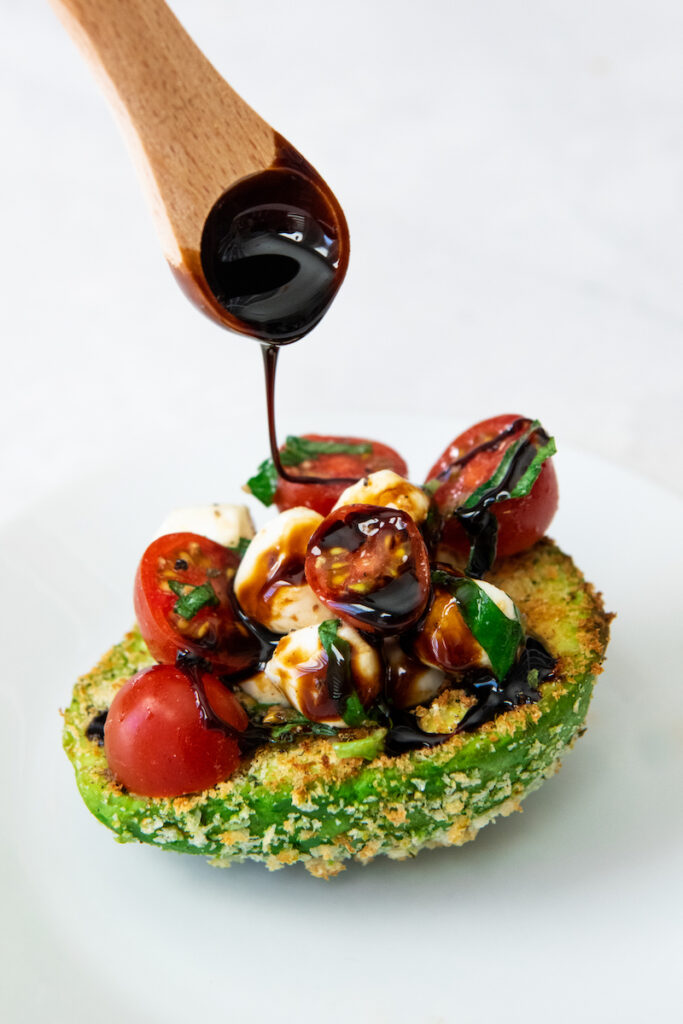 Balsamic glaze is drizzled on top of a fried avocado stuffed with caprese filling.