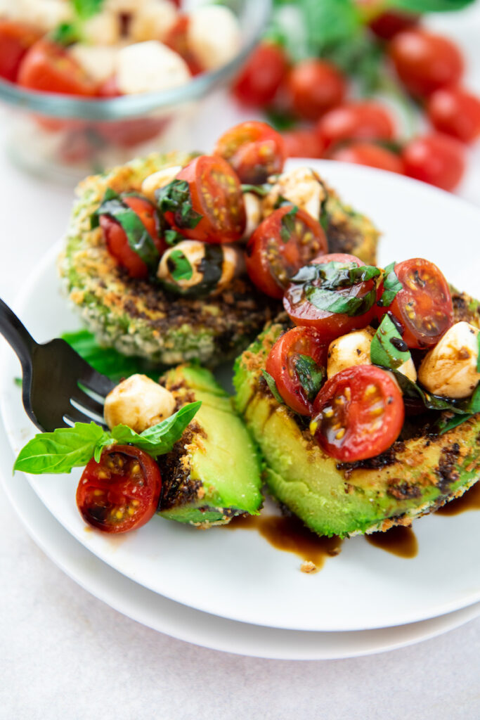 A fork is taking a bite size piece out of a caprese stuffed avocado.