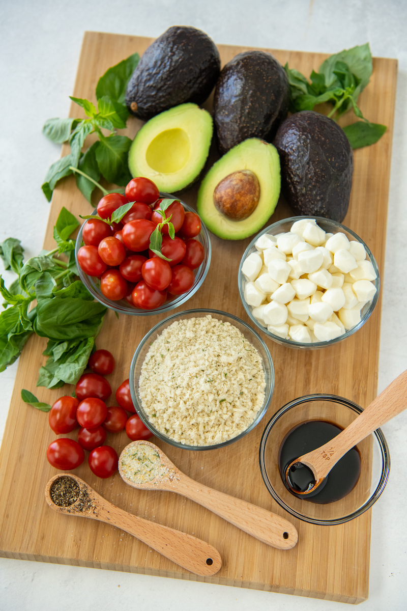 The ingredients for capers stuffed avocados are placed on a wooden cutting board.