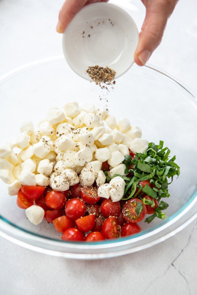 Cheese, tomatoes and basil are in a glass bowl and seasoned with salt and pepper.