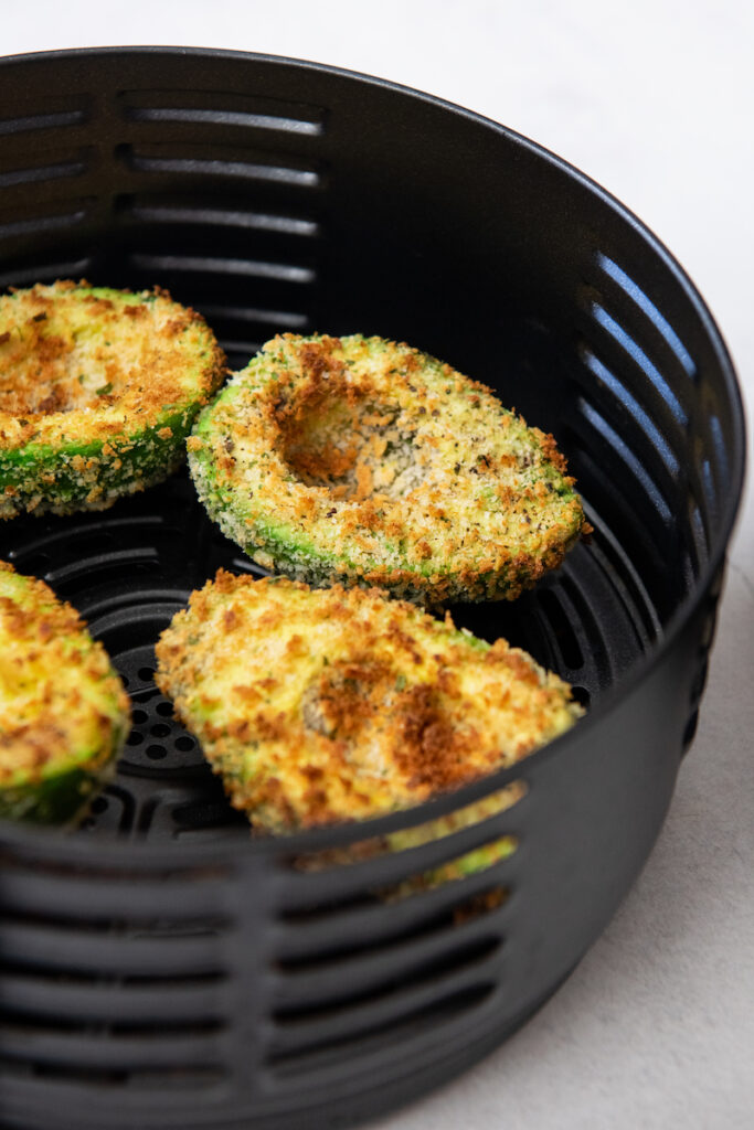 Four avocado halves are in a black air fryer basket.