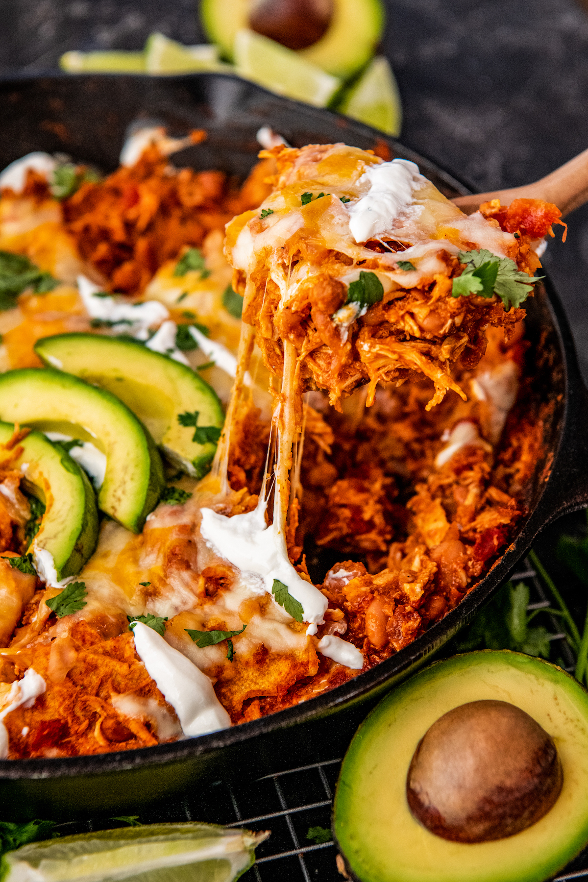 A large spoon is scooping out a portion of chicken enchiladas from a black skillet.