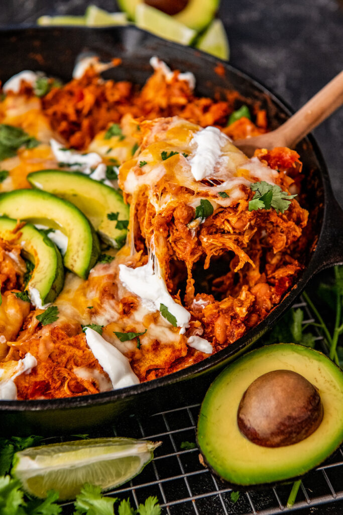 A serving of enchiladas is being taken out of the skillet with a large spoon.