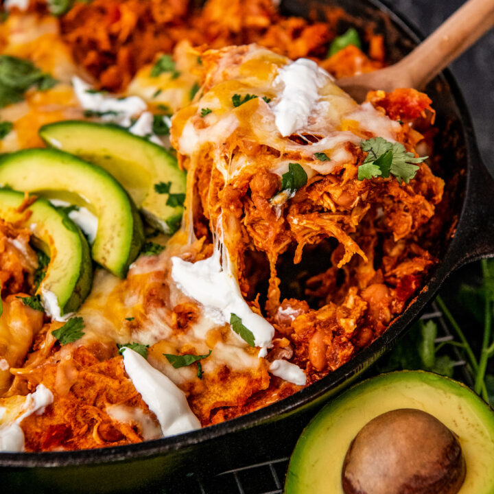 A serving of enchiladas is being taken out of the skillet with a large spoon.