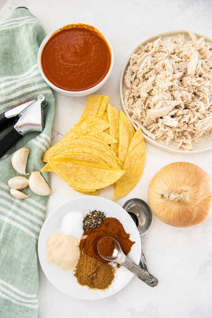 The ingredients for chicken enchiladas are placed on a white surface.