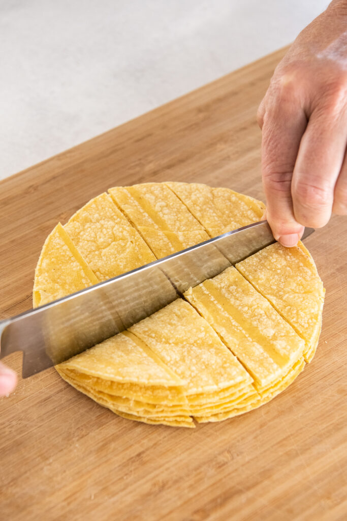 Corn tortillas are being sliced with a large knife.