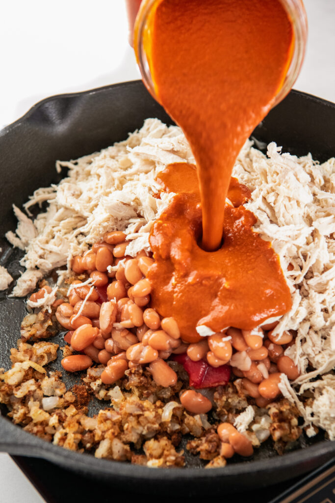 Red enchilada sauce is poured on top of beans and Rotel in the skillet.
