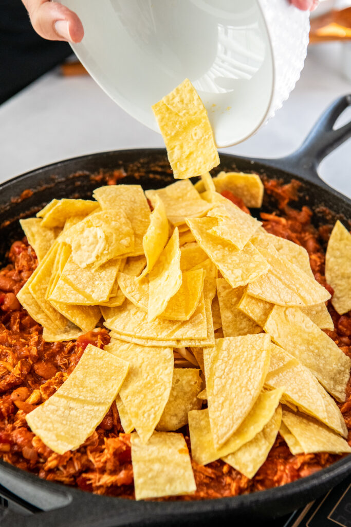 Tortilla strips are being placed into the skillet.