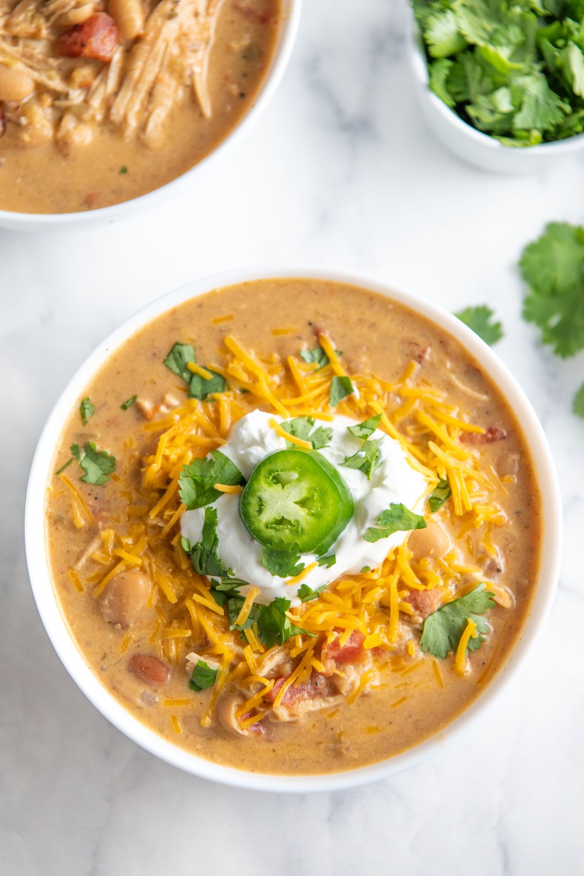 A white bowl filled with white chicken choli and topped with sour cream, cheddar cheese and a slice of jalapeno.