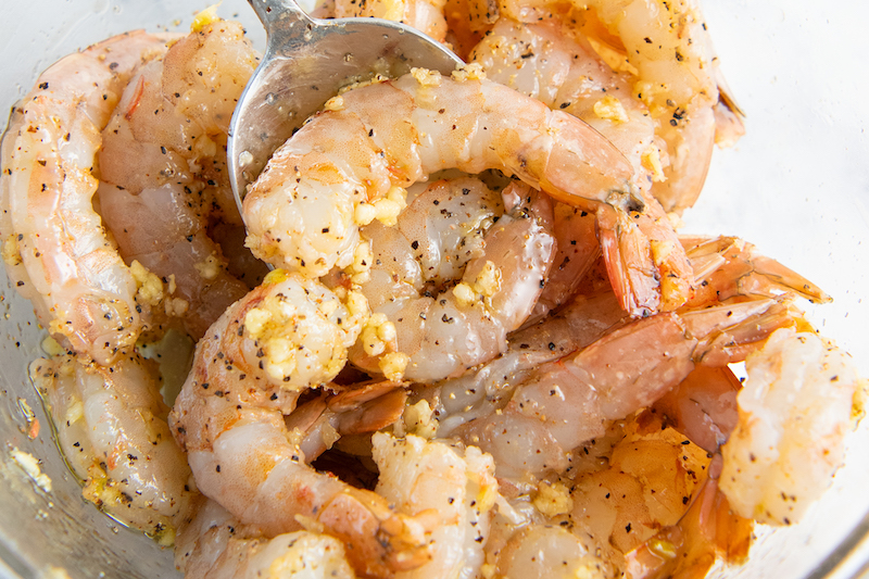 A metal spoon is picking up a shrimp from the glass bowl.
