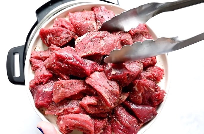 Beef tips on a plate with salt and pepper and tongs moving a piece.