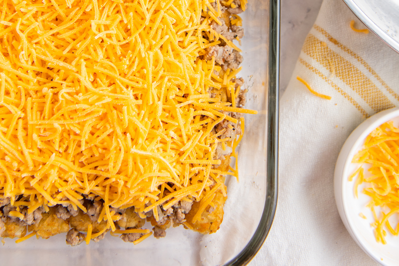 Shredded cheddar cheese is covering the meat and tots.
