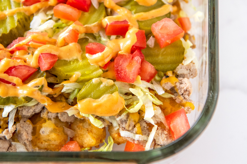 The toppings for cheeseburger casserole have been placed on top of the melted cheese.
