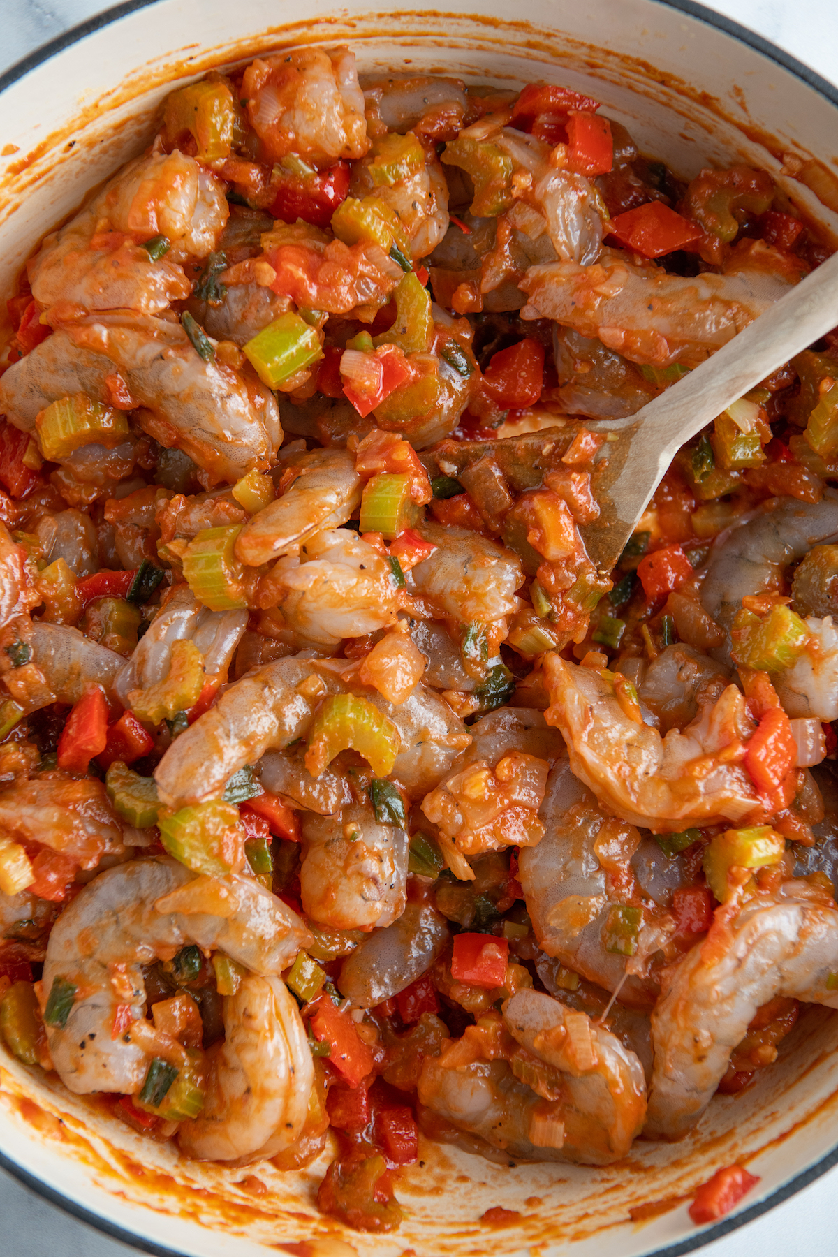 Raw shrimp in a skillet with red sauce and bell peppers. 