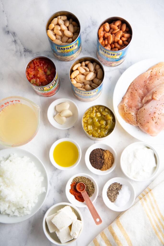 Picture of 3 cans of beans, can of tomatoes, seasonings, chicken broth, chicken breast, chopped onion, cream cheese and sour cream.