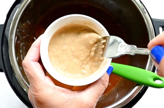 A slurry of gravy and cornstarch being whisked with a fork in a bowl over an instant pot.