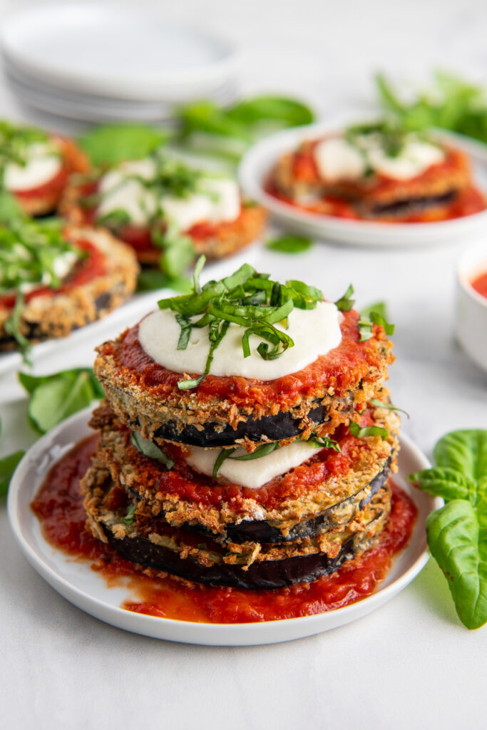 Eggplant Parmesan topped with mozzarella, sauce and basil stacked on a plate 