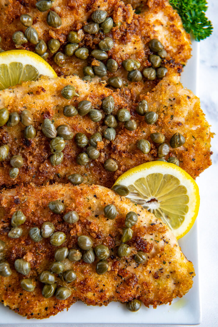 Chicken Piccata with capers on a white plate with lemon slices
