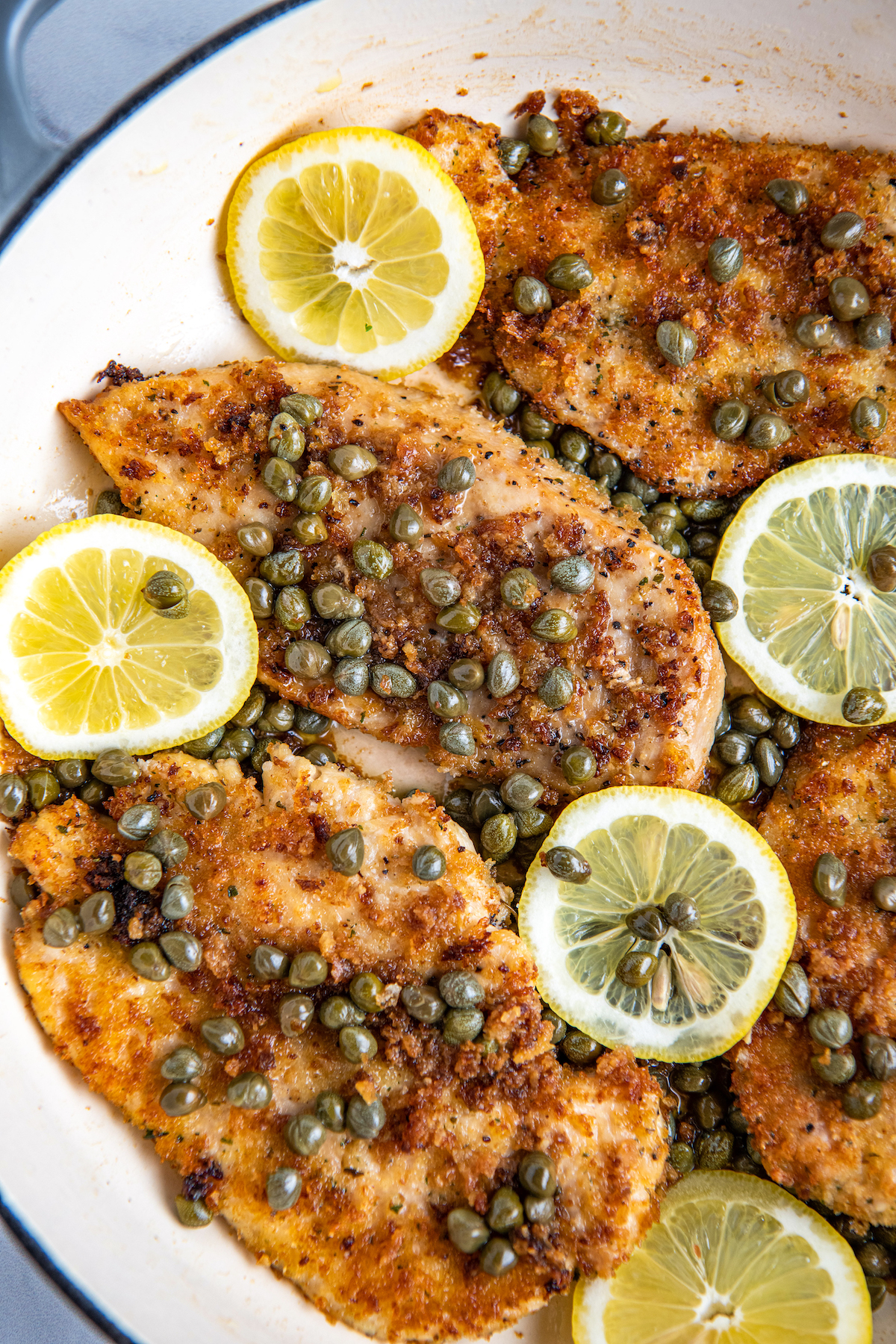 Chicken piccata in a white cooking pan with lemon slices