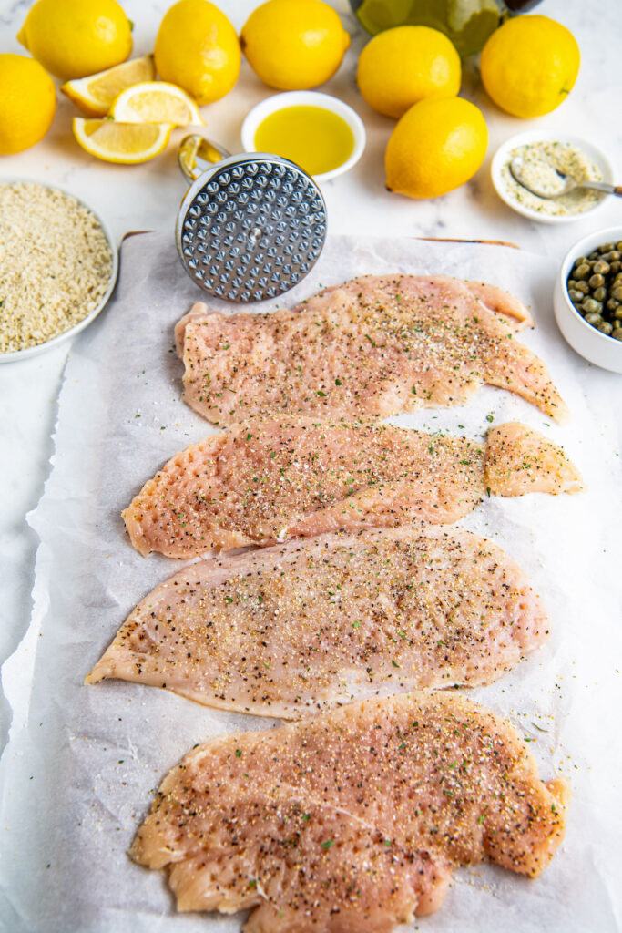 Raw chicken breast with seasoning and lemons and capers