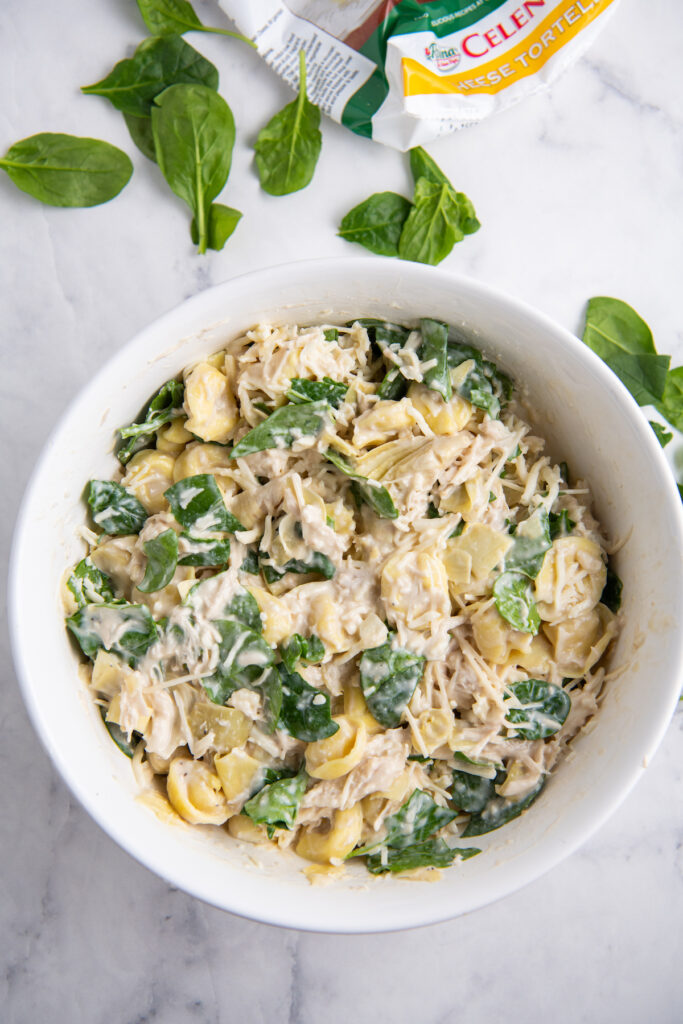 Mixing bowl filled with tortellini, spinach, artichoke hearts, alfredo sauce and cheese.