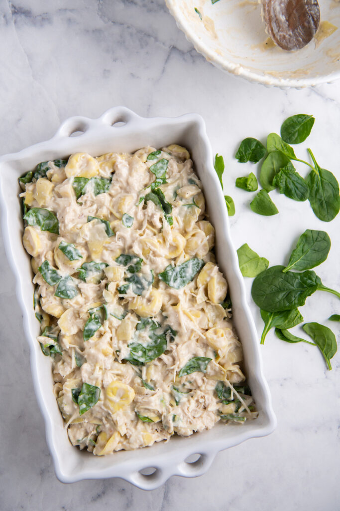 Tortellini, spinach, artichoke hearts, cheese with alfredo sauce in a casserole dish.